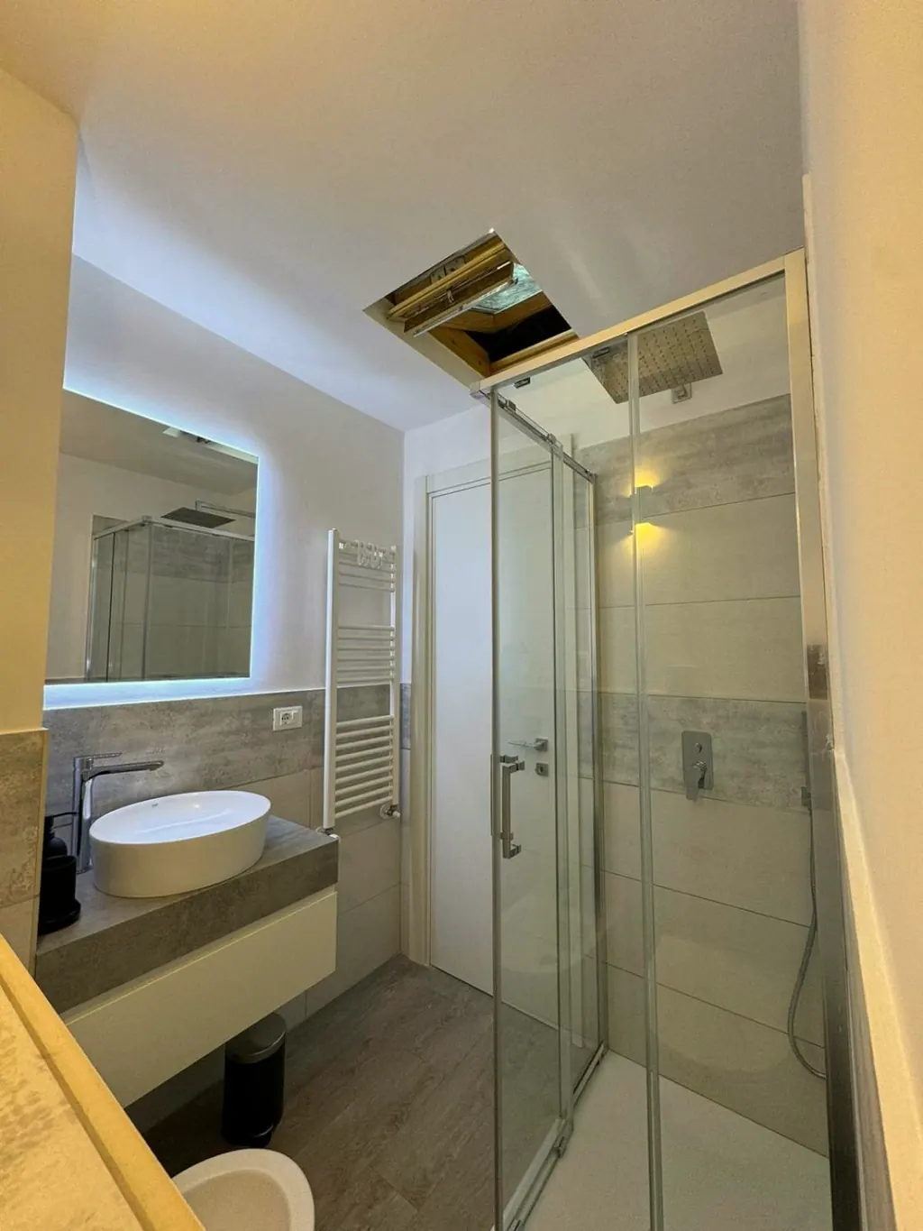 Bagno con doccia in cristallo sotto il lucernario e lavabo in appoggio