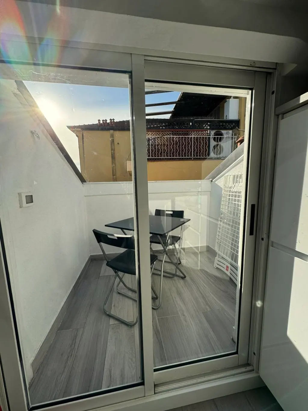 Porta finestra aperta su un piccolo balcone con tavolino e due sedie
