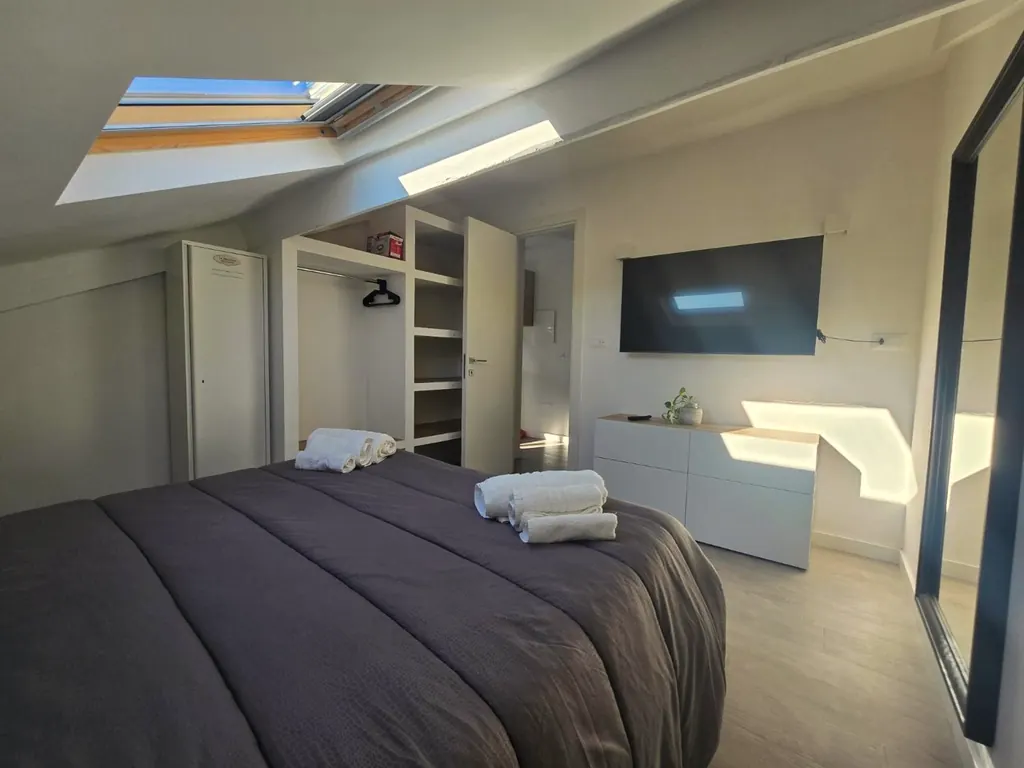 Letto matrimoniale di fronte ad armadio aperto, cassettiera e televisore a parete