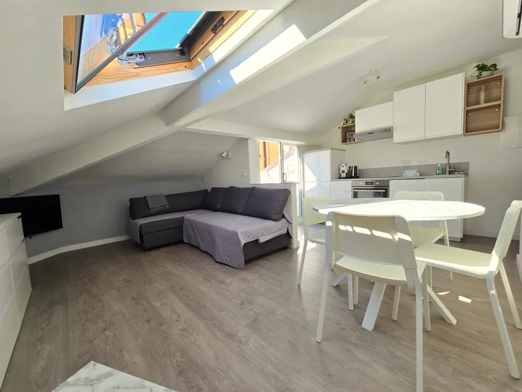 Soggiorno mansardato con lucernari, divano letto, tavolo bianco e cucina sullo sfondo